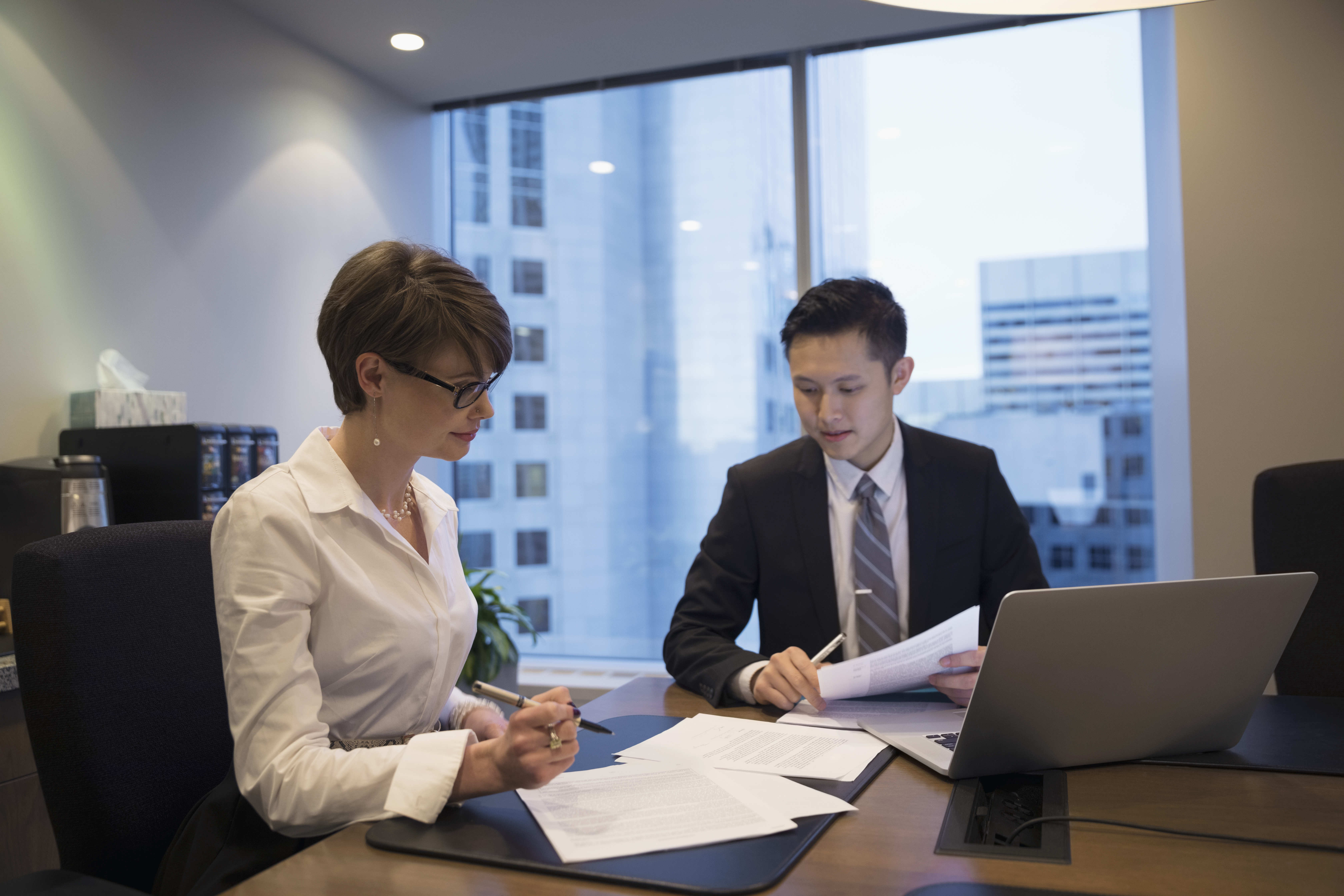 business colleagues in office discussing paperwork and content on laptop